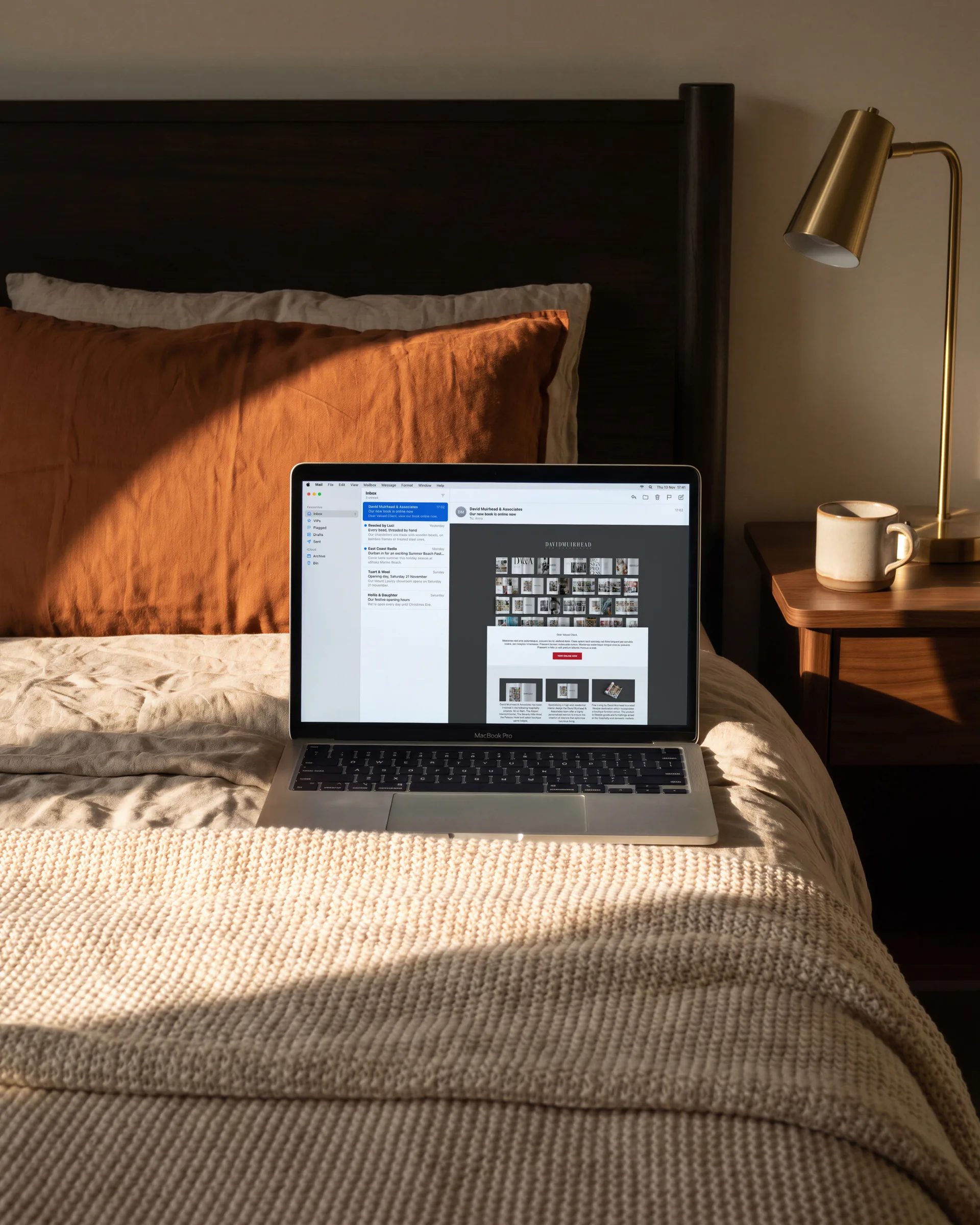 David Muirhead’s email announcing a new book, open on a laptop on a bed, a mug and a brass lamp beside it.