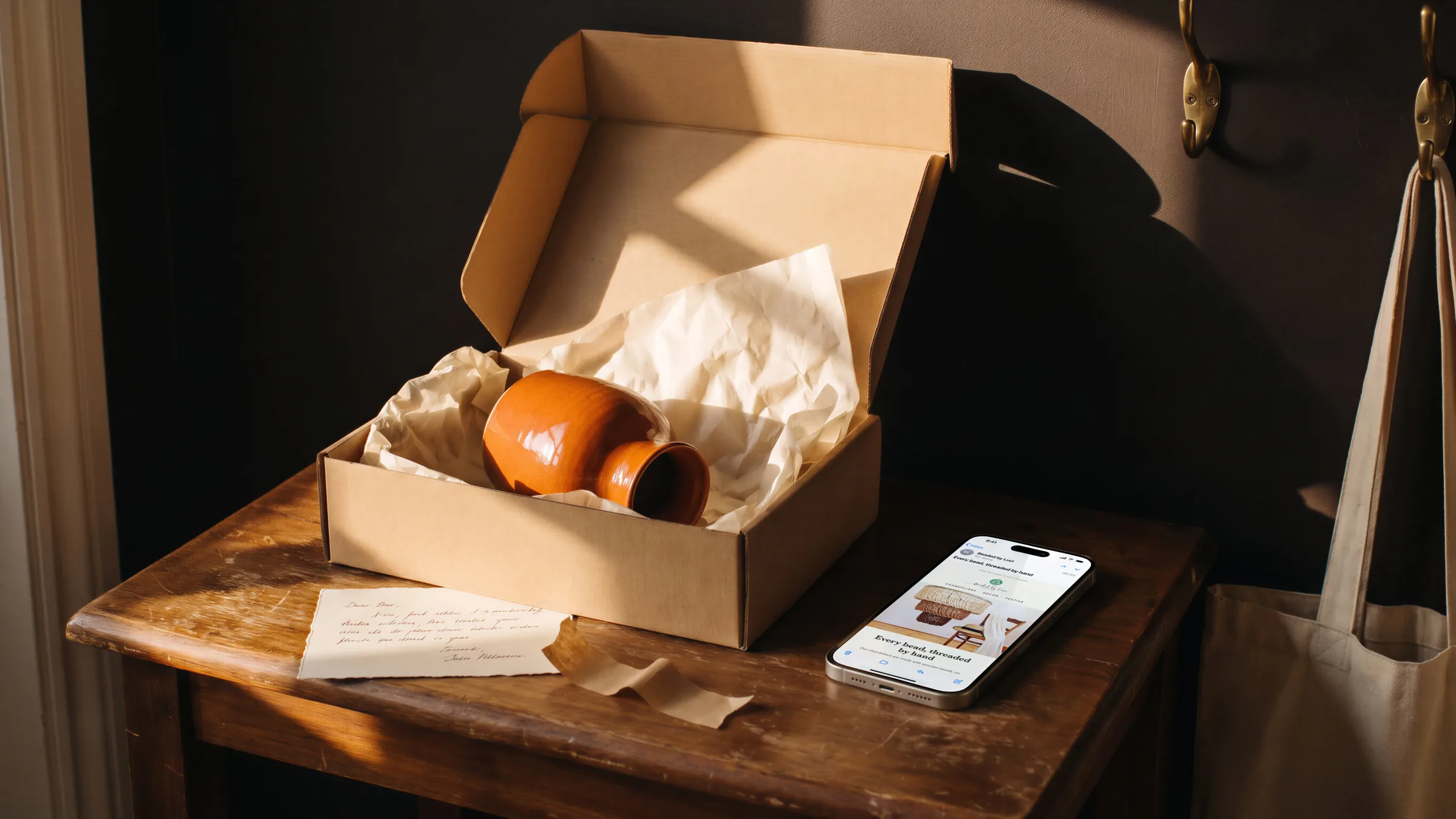Beaded by Luci’s newsletter on a phone on a hall table beside an opened box holding an orange vase in tissue.