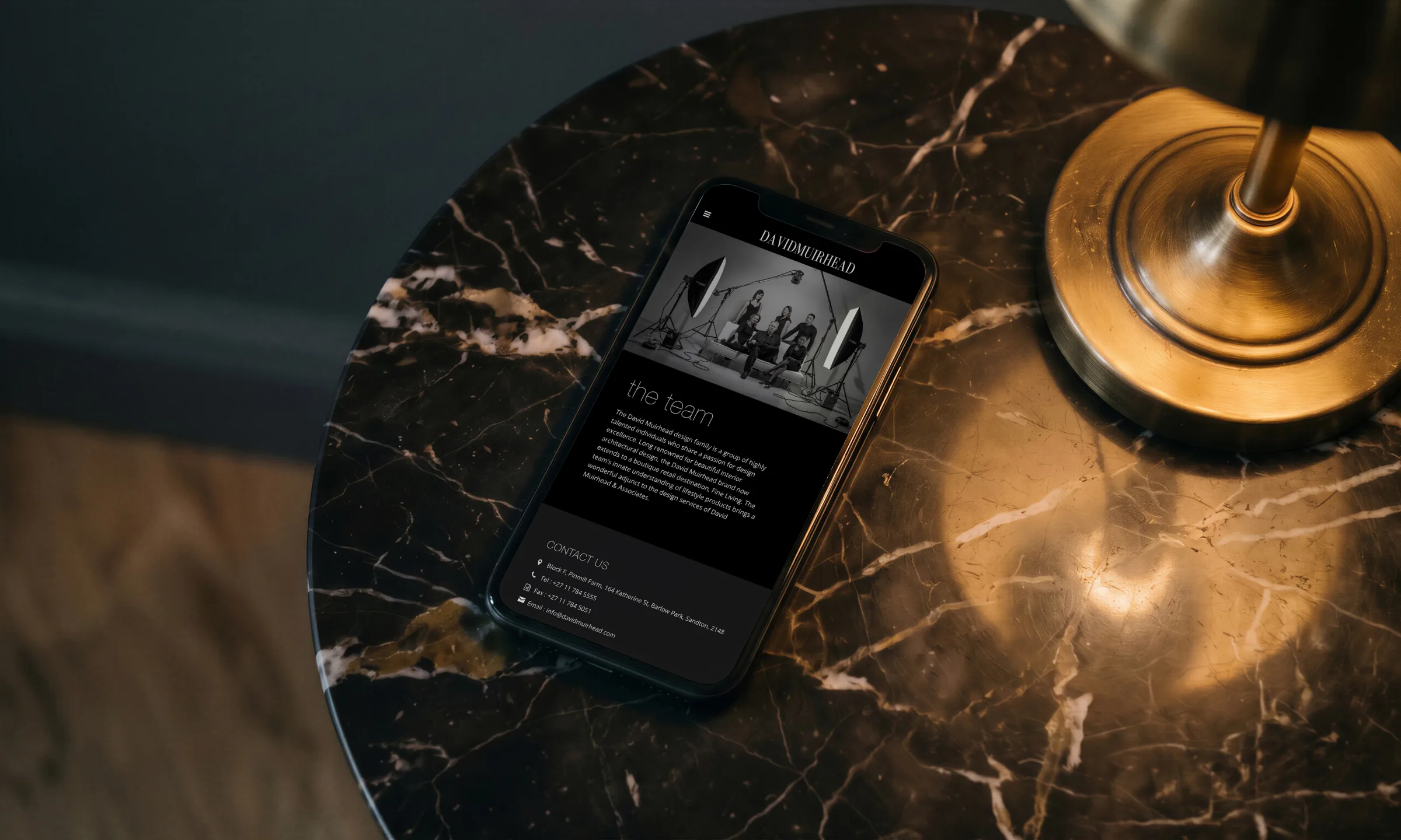 The website on a laptop on a marble table in a low-lit lounge, the whippet on screen.