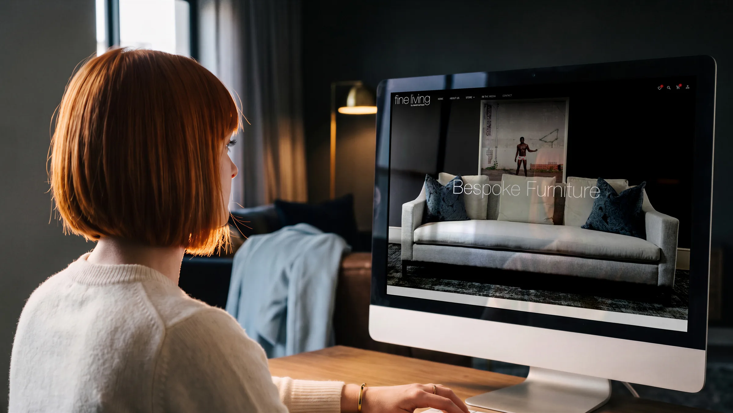 The home page on a laptop in a café: the red sofa under Boutique Collection, a hand on the trackpad.