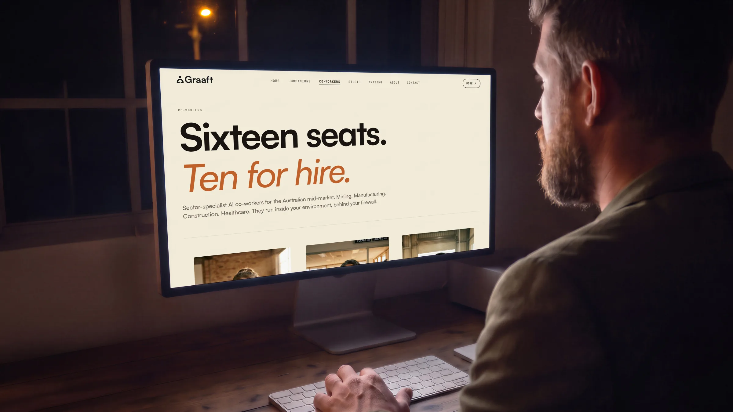 A man at a large display in a studio at night, the co-workers page from its top, nav and all, on its screen.