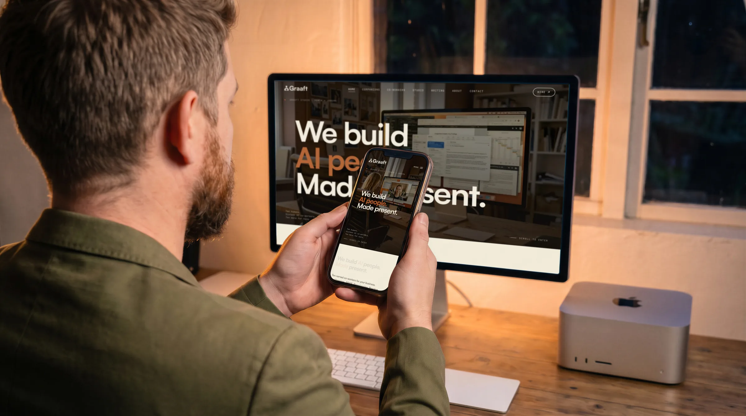 At night, a man holding a phone up in front of a large display, the home page on both.