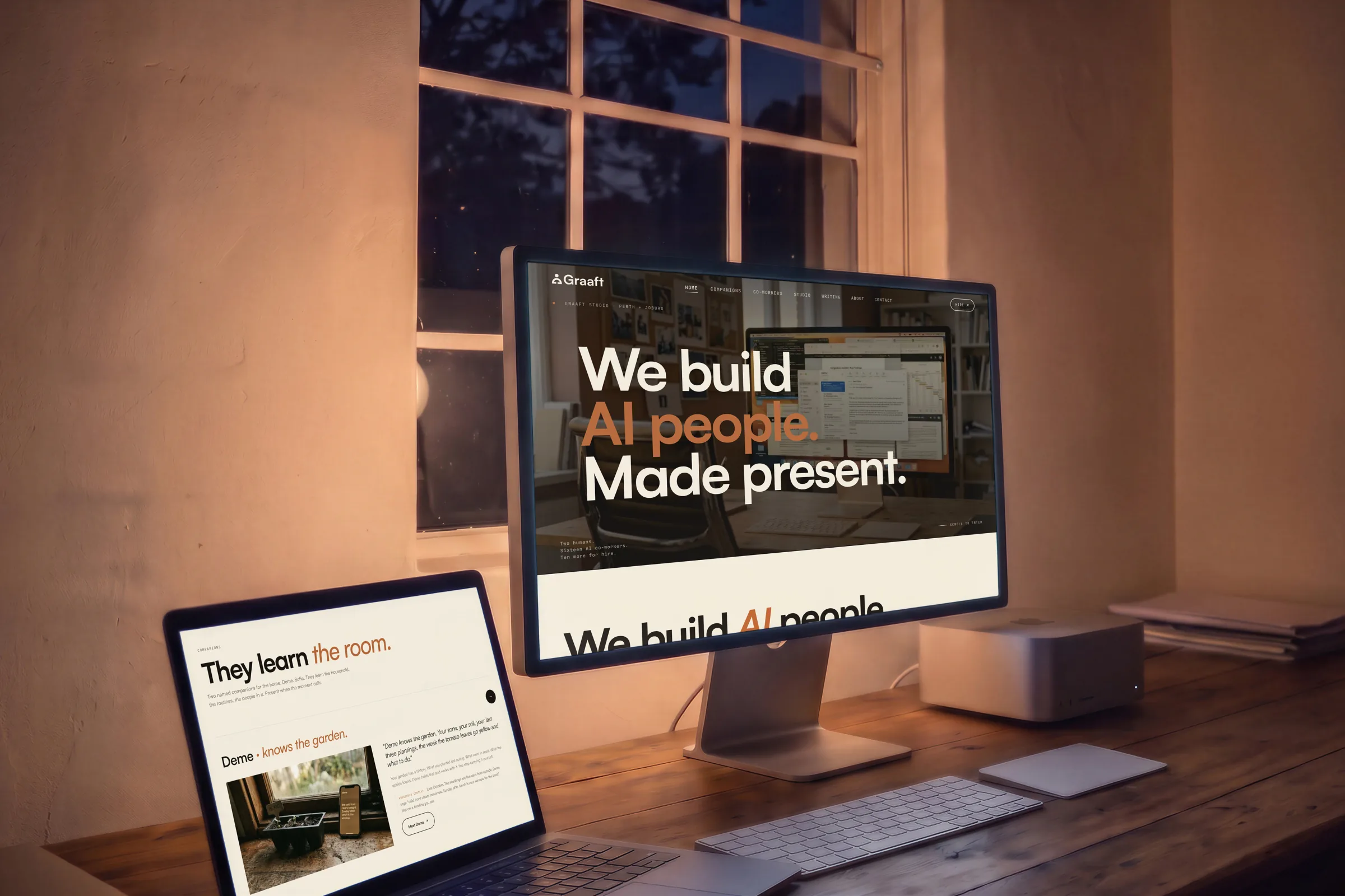 A display and an open laptop side by side on a timber desk at night, the home page’s hero on one and They learn the room. on the other.
