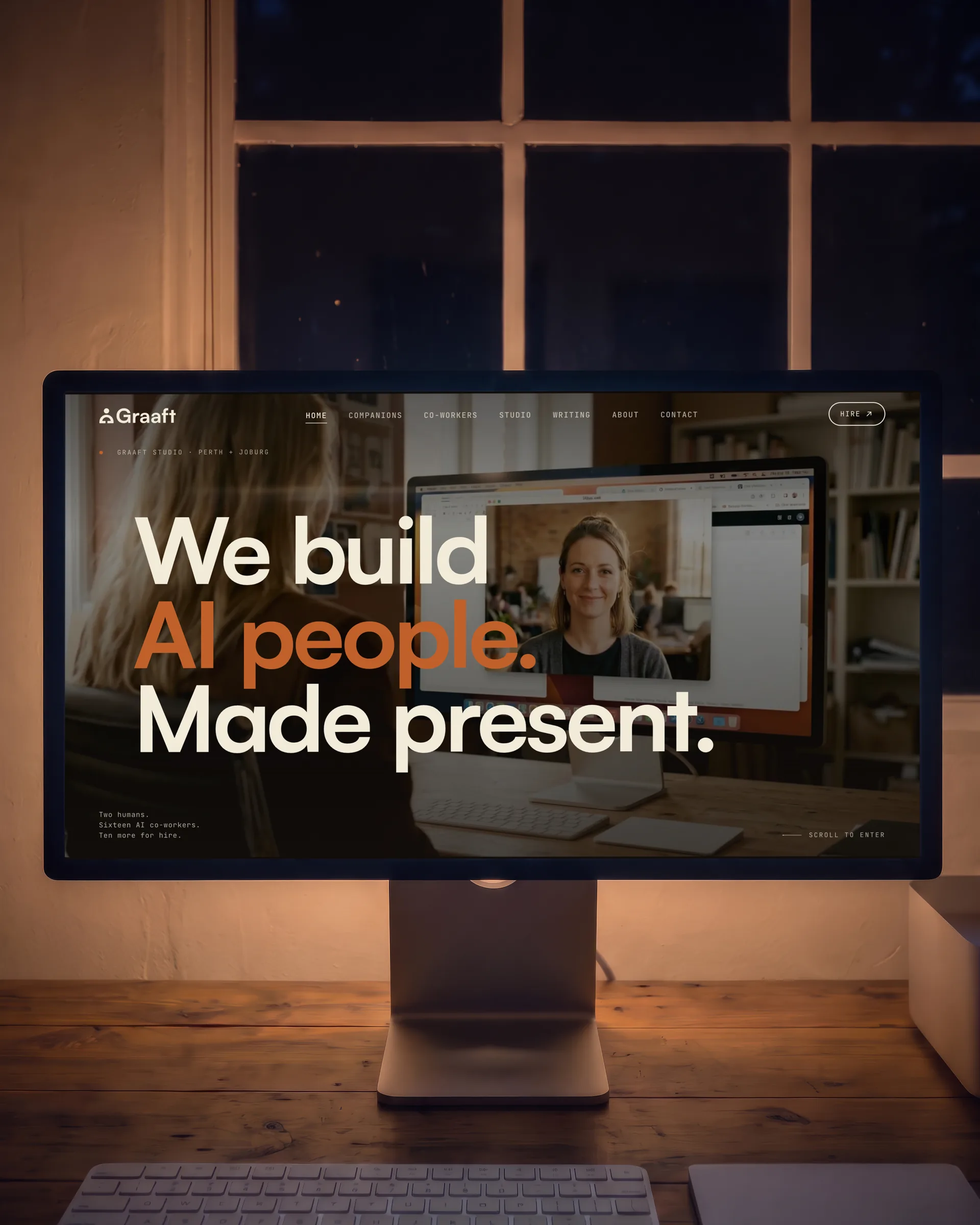 At night, a large display on a timber desk showing the graaft.ai home page, the window’s bars behind.
