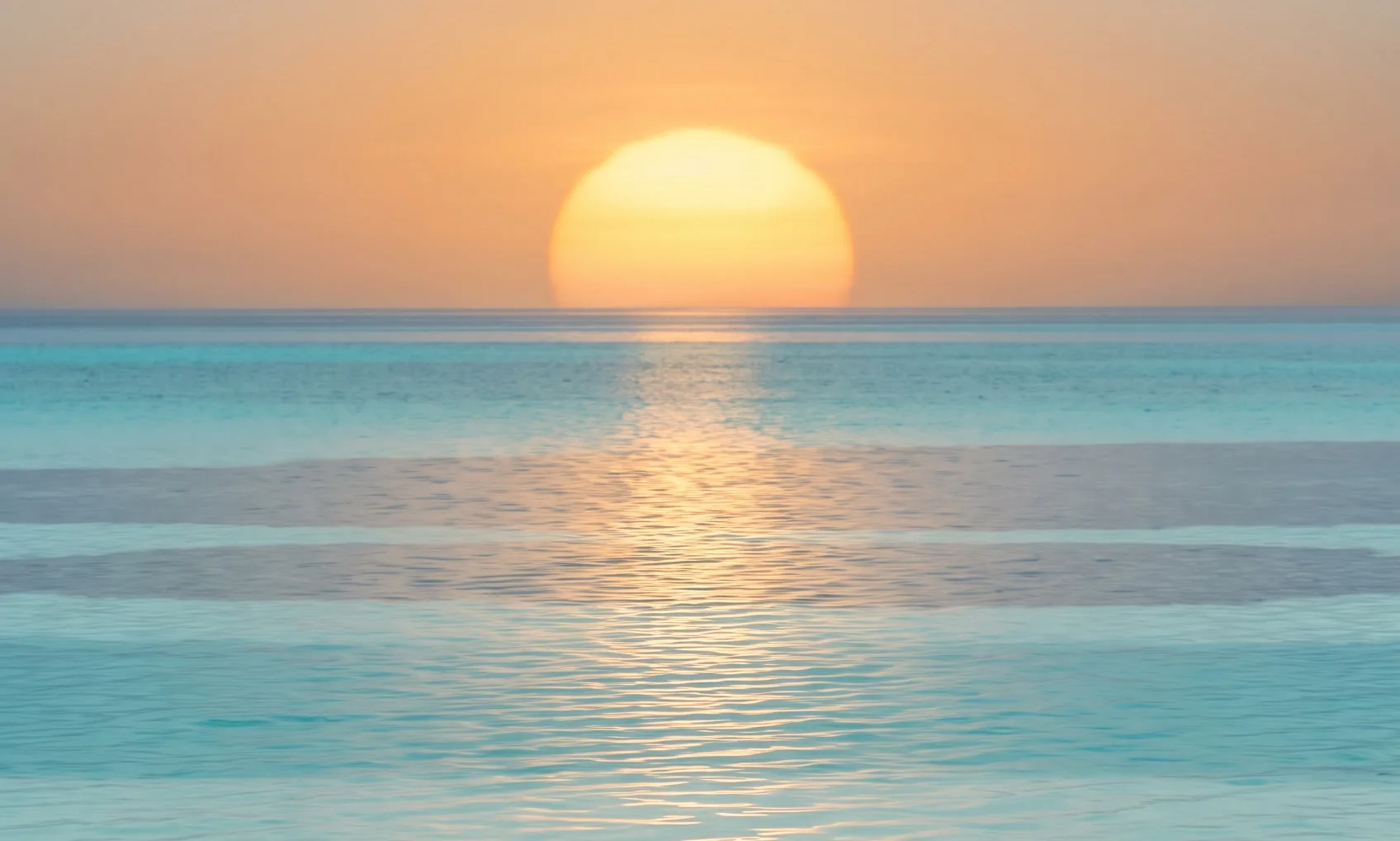 A low gold sun over a shallow turquoise lagoon, the place the logo pictures.