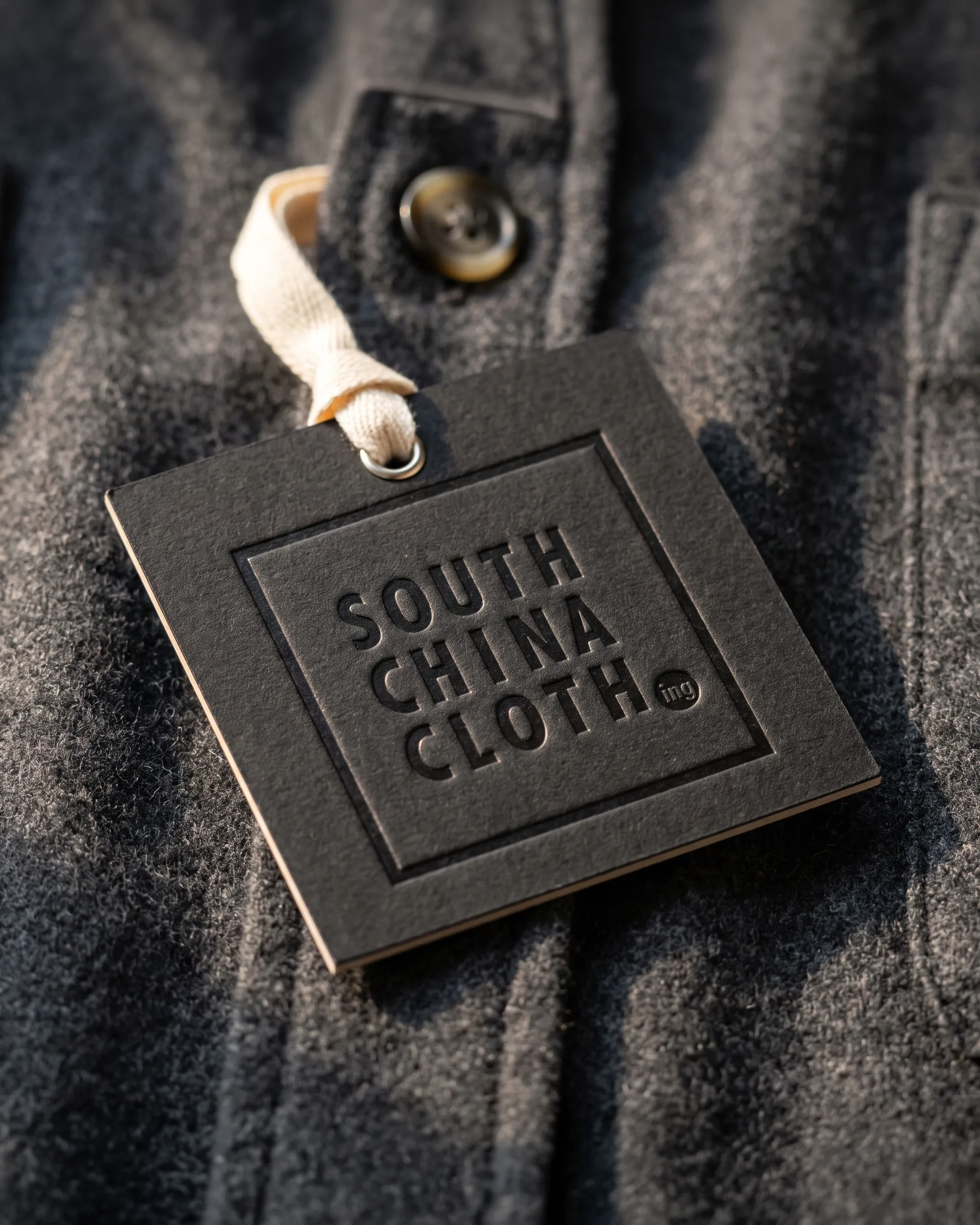 A black swing tag, the logo blind debossed, hanging from a grey flannel jacket.