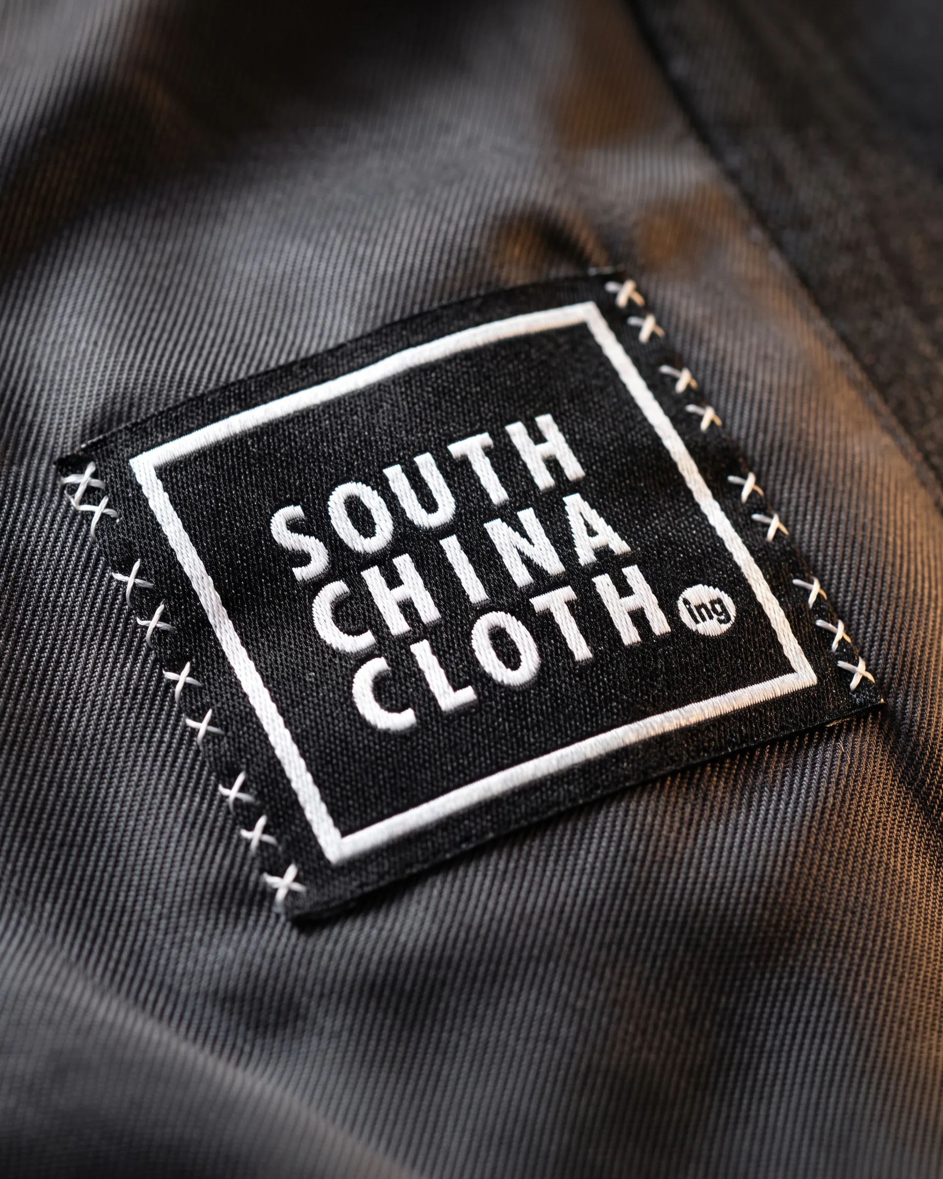 A black woven label with the boxed logo, cross-stitched into a charcoal jacket lining.