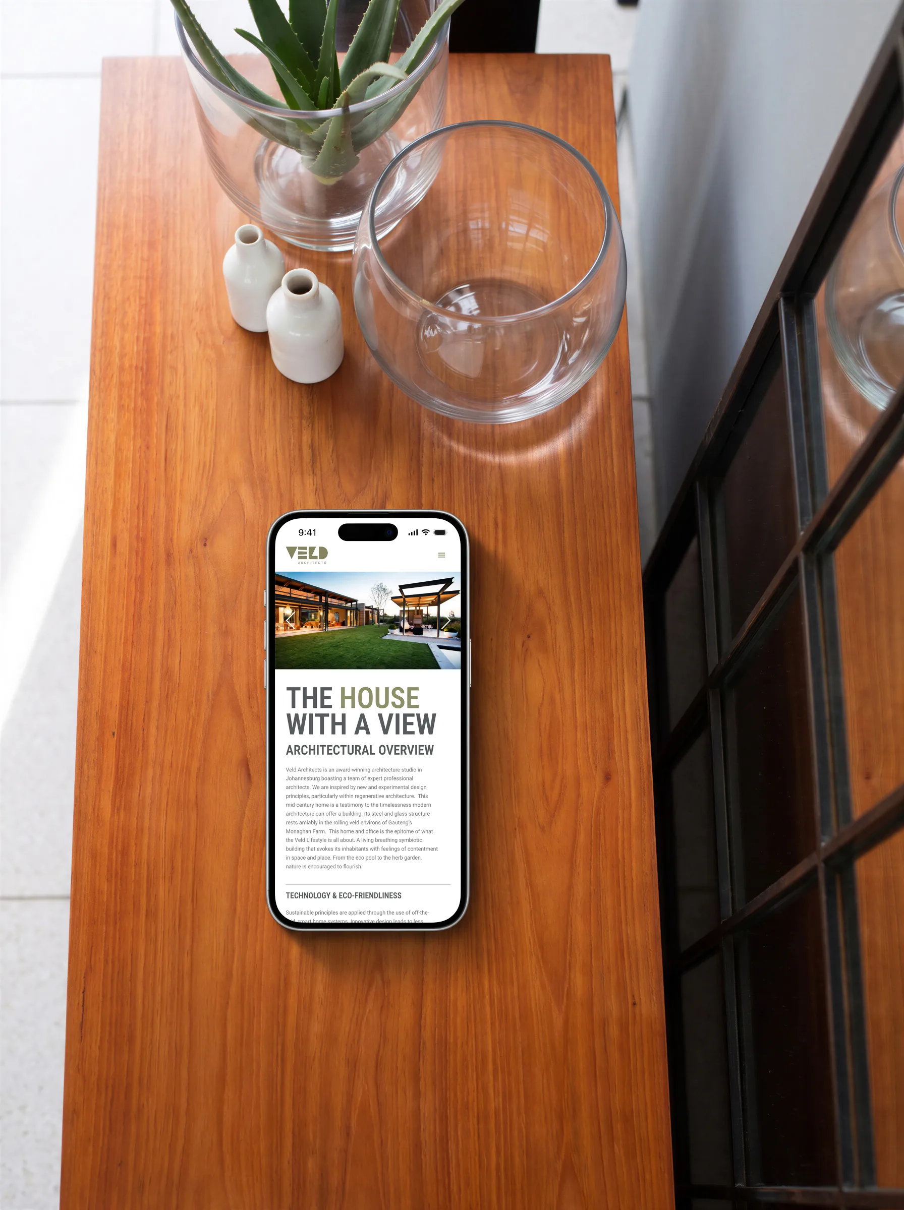 The House with a View’s page on a phone, from above, on the house’s timber sideboard beside its glass vessels and arched mirror.