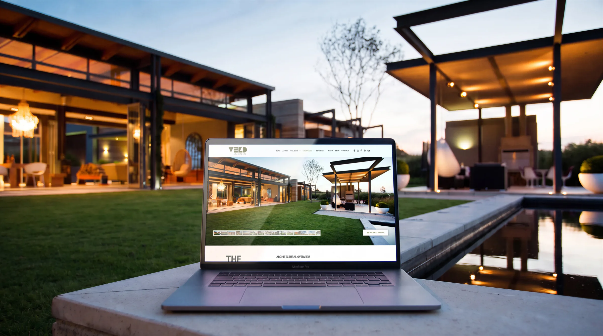 The House with a View’s page on a laptop on the pond’s ledge, the house itself behind it at dusk.