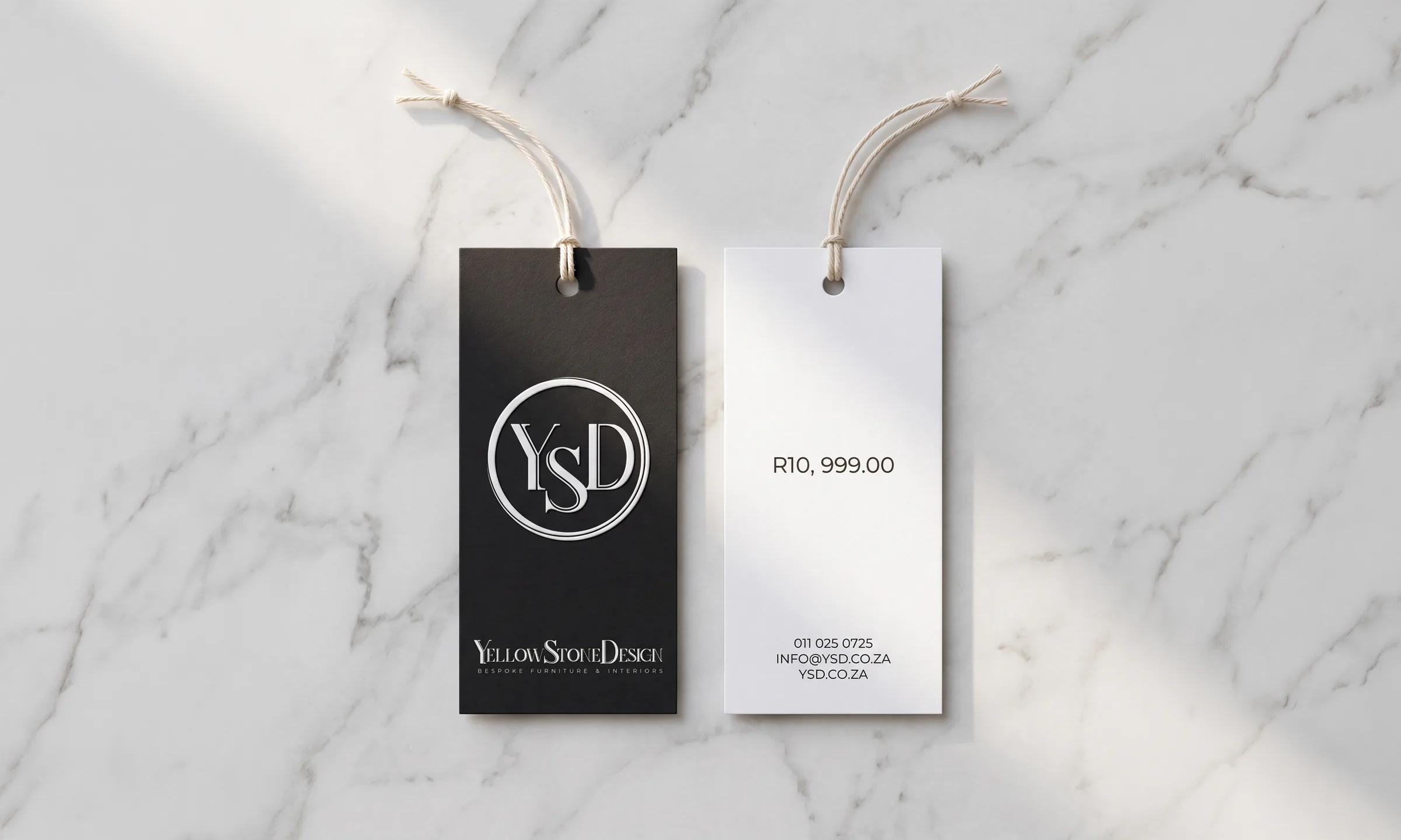 Two swing tags on pale marble, one face up with the monogram, one turned over with the price and contacts.